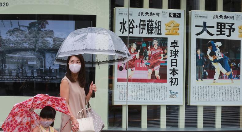 People wearing face masks to protect against the spread of the coronavirus walk past extra papers reporting on Japanese gold medalists at Tokyo Olympics, in Tokyo Tuesday, July 27, 2021.
