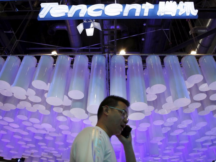 A man uses a mobile phone in front of a logo of Tencent at the Global Mobile Internet Conference (GMIC) 2015 in Beijing.