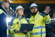 Male and Female Industrial Engineers Talk with Factory Worker while Using Laptop. They Work at the Heavy Industry Manufacturing Facility.