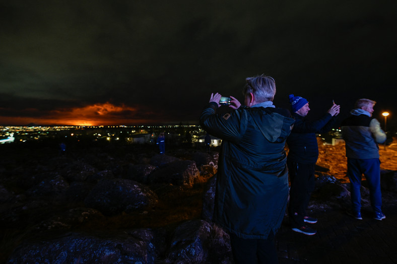 Ludzie na obrzeżach Reykjaviku robią zdjęcia i selfie z pomarańczowym niebem, gdy stopiona lawa wypływa ze szczeliny na półwyspie Reykjanes na północ od ewakuowanego miasta Grindavik