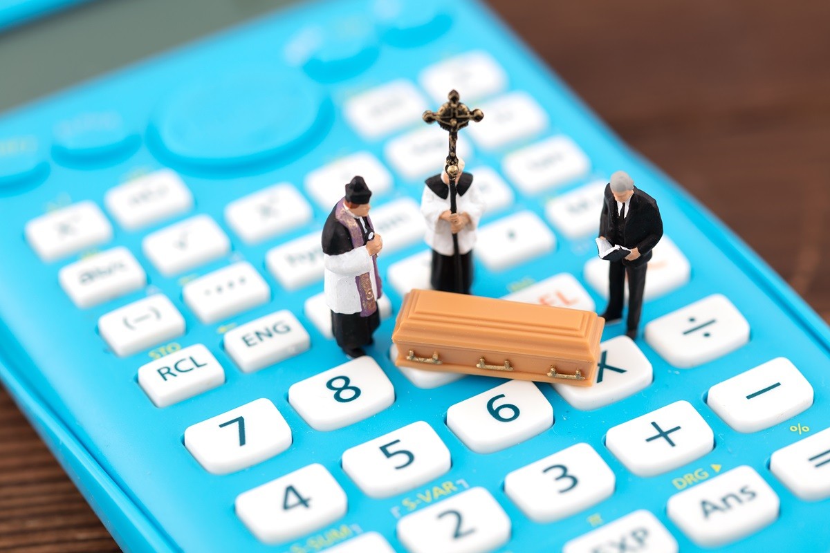 Na kalkulatorze stoi ksiądz i żałobnik nad trumną