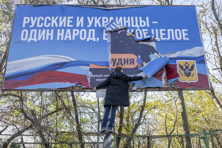Mężczyzna w Chersoniu usuwa baner z czasu rosyjskiej okupacji, który głosi "Rosjanie i Ukraińcy to jeden naród, jedna całość"