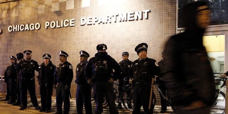 A protester walks past a line of police officers standing guard in front of the District 1 police headquarters in Chicago, November 24, 2015.