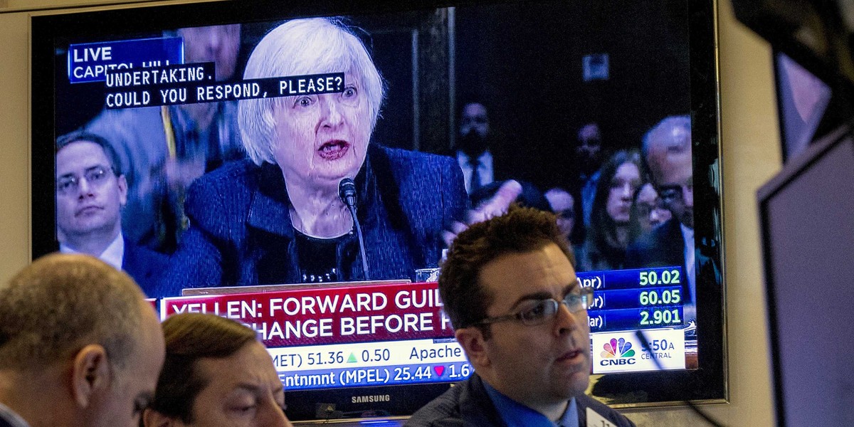 Traders work on the floor of the New York Stock Exchange, as a television screen displays Federal Reserve Chair Janet Yellen testifying before Congress, February 24, 2015.