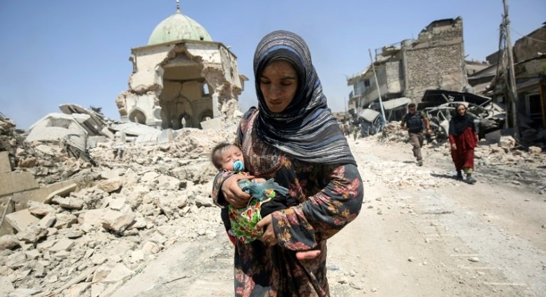 An Iraqi woman carrying a child walks by the destroyed Al-Nuri Mosque as she flees the Old City of Mosul on July 5, 2017