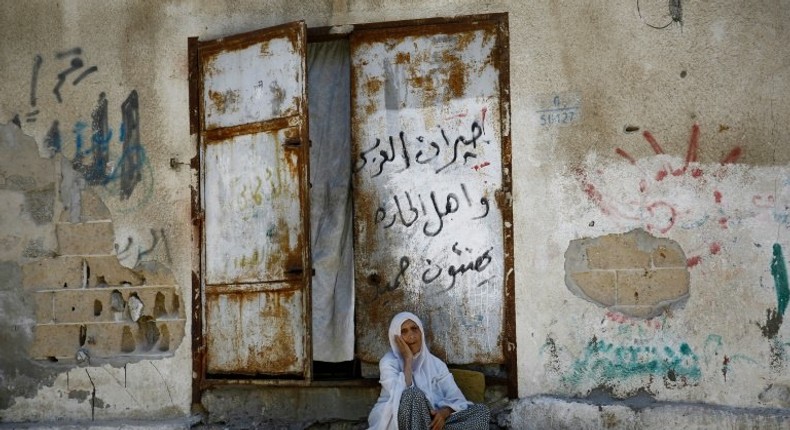 An elderly Palestinian woman sits in front of her house in Gaza City