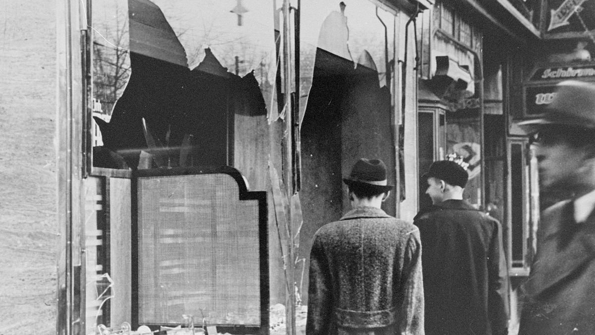 Germans pass by the smashed windows of a Jewish-owned shop. The aftermath of Kristallnacht (Night of