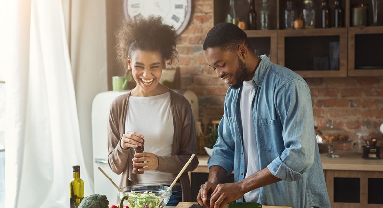 Laughing black couple preparing salad in kitchen