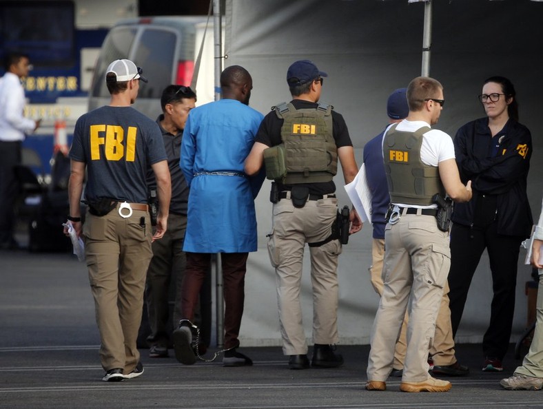 Federal agents hold a detainee, second from left, at a downtown Los Angeles parking lot after predawn raids that saw dozens of people arrested in the L.A. area on Thursday, Aug. 22, 2019 [AP Photo/Reed Saxon]
