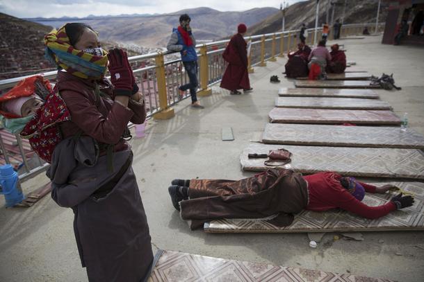 Ethnic Tibetan woman, carrying her baby on the back, prays at a monastery above the Larung Wuming Bu