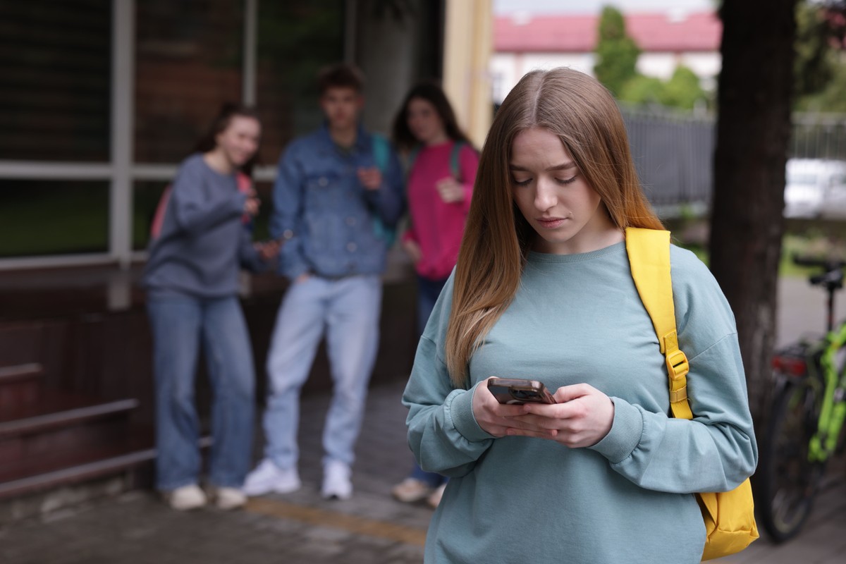 Nastolatka z telefonem w ręku, w tle grupa kolegów