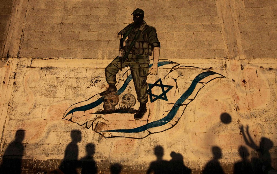 The shadows of Palestinian children are cast against a wall as they play with a ball in front of an anti-Israel mural in Gaza City