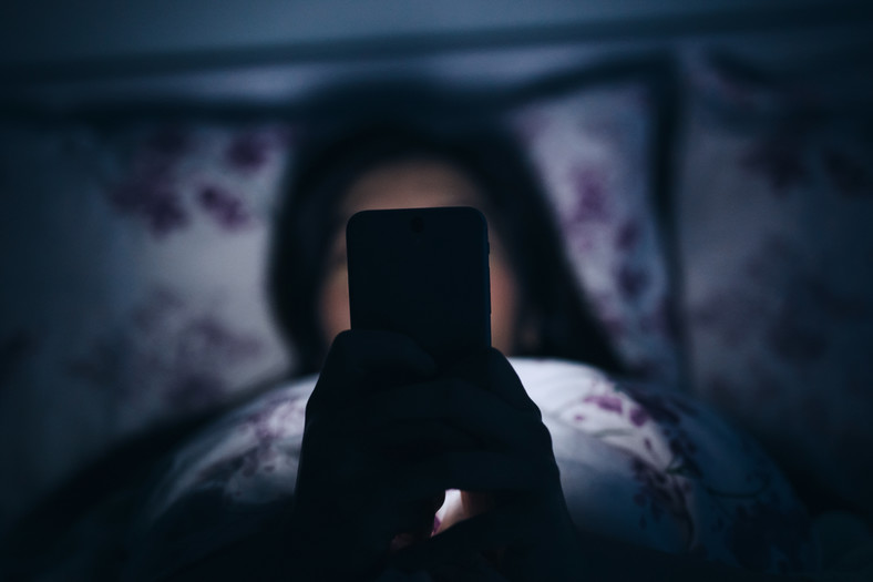 Kobieta z telefonem w łóżku (zdj. ilustracyjne)