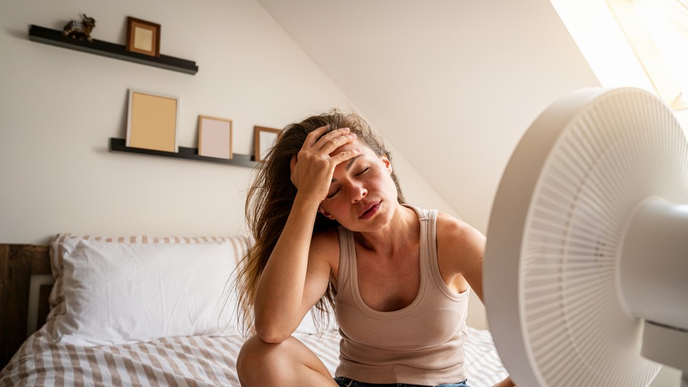 Overheated woman trying to cool down with fan at home