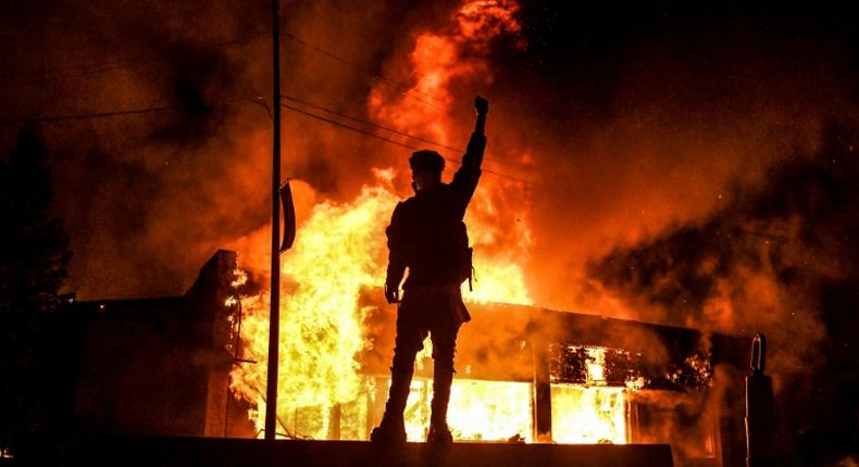 Un manifestant devant un bâtiment incendie dans la ville américaine de Minneapolis dans la nuit du 29 au 30 mai 2020