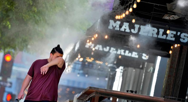 A man wipes his brow as he walks under misters, on July 13, 2023, in downtown Phoenix.Matt York/AP