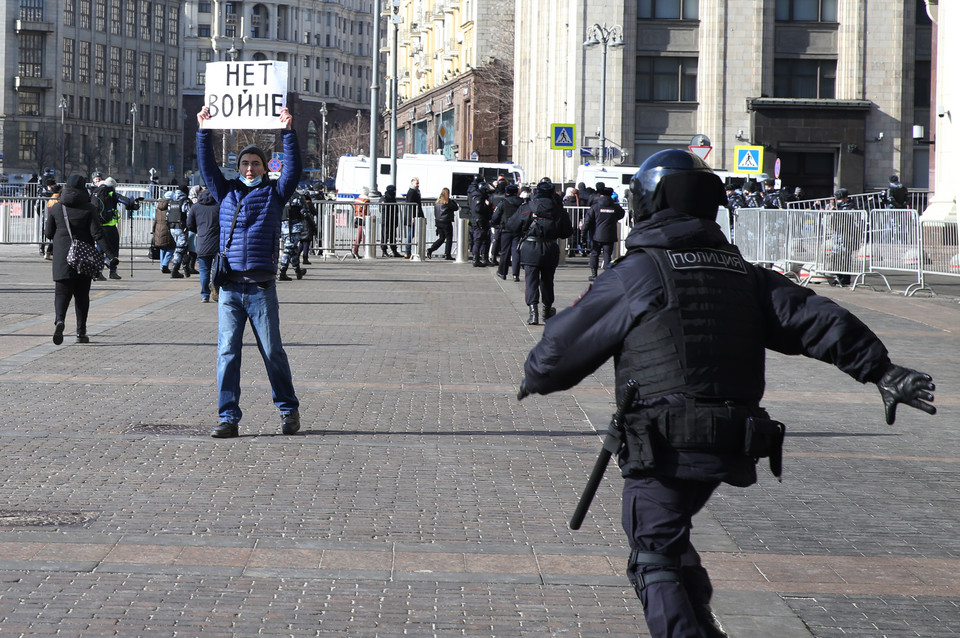 Funkcjonariusz rosyjskiej policji biegnie do zatrzymania mężczyzny trzymającego plakat z napisem: "Nie dla wojny".