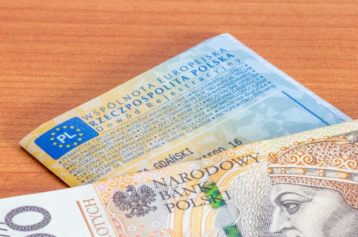 Polski dowód rejestracyjny pojazdu oraz banknot 200 zł leżące na drewnianym blacie