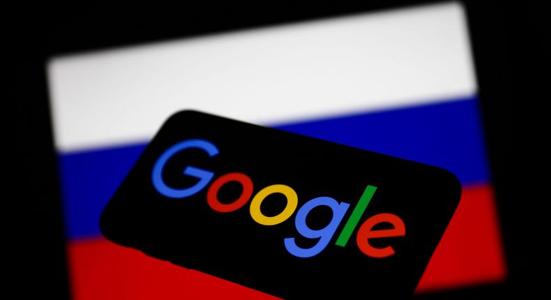Google logo displayed on a phone screen and Russian flag displayed on a screen in the background.