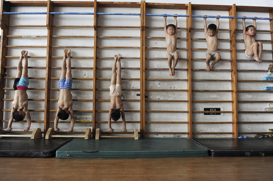 Young gymnasts, in a class consisting of four to seven-year-olds, stretch themselves on wooden bars at the gymnastics hall of a sports school in Jiaxing, Zhejiang province August 10, 2010.