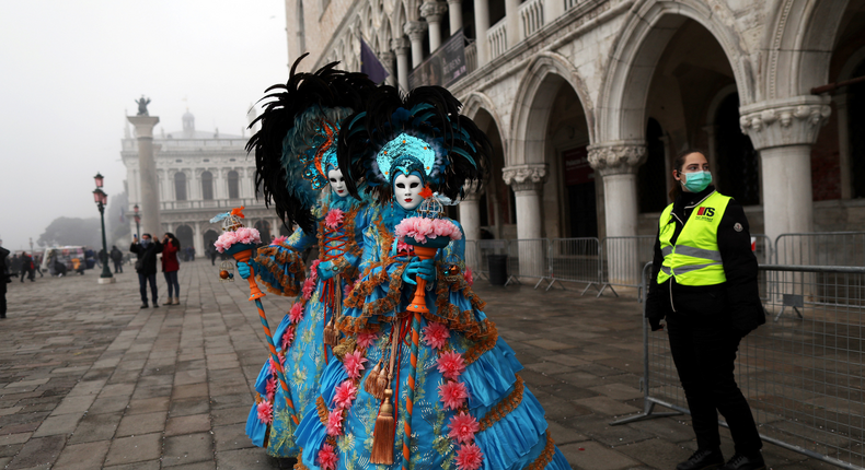 A policewoman wearing a protective mask stands next to carnival revellers at Venice Carnival, which the last two days of, as well as Sunday night's festivities, have been cancelled because of an outbreak of coronavirus, in Venice, Italy February 23, 2020.