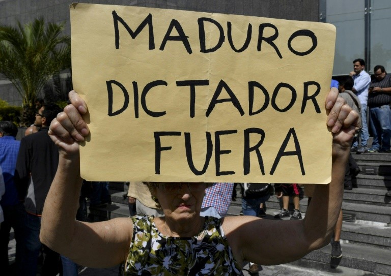 The sign held by an anti-government activist at the rally where Juan Guaido spoke reads "Maduro dictator out"