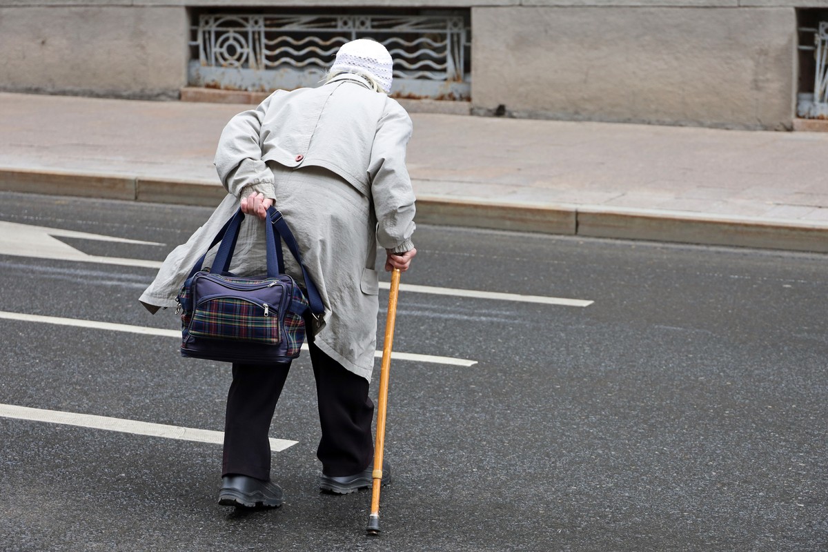 Starsza kobieta z laską przechodzi przez ulicę