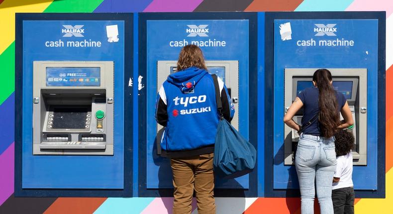 People make cash withdrawals from Halifax cash machines, or ATMs, set on a colourful wall in Manchester, United Kingdom.