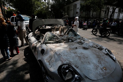 People are seen next to a damaged car after an earthquake in Mexico City