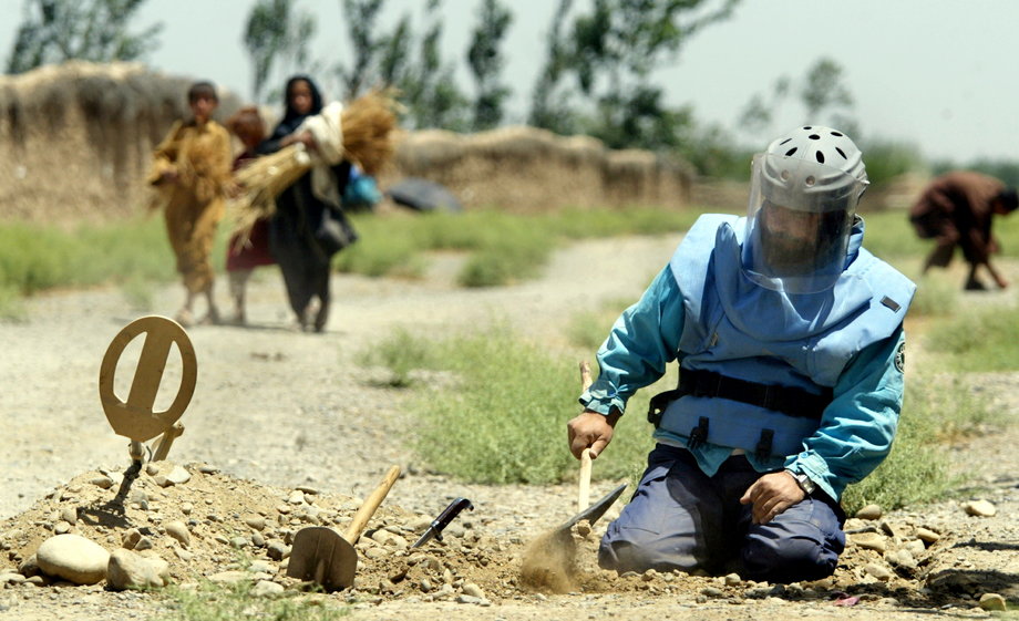 An Afghan sapper searches for antitank mines as peasants make their way through the unsearched area in Bagram valley, near a coalition joint task force base, 50 kms (31 miles) north of Kabul, June 29, 2003.