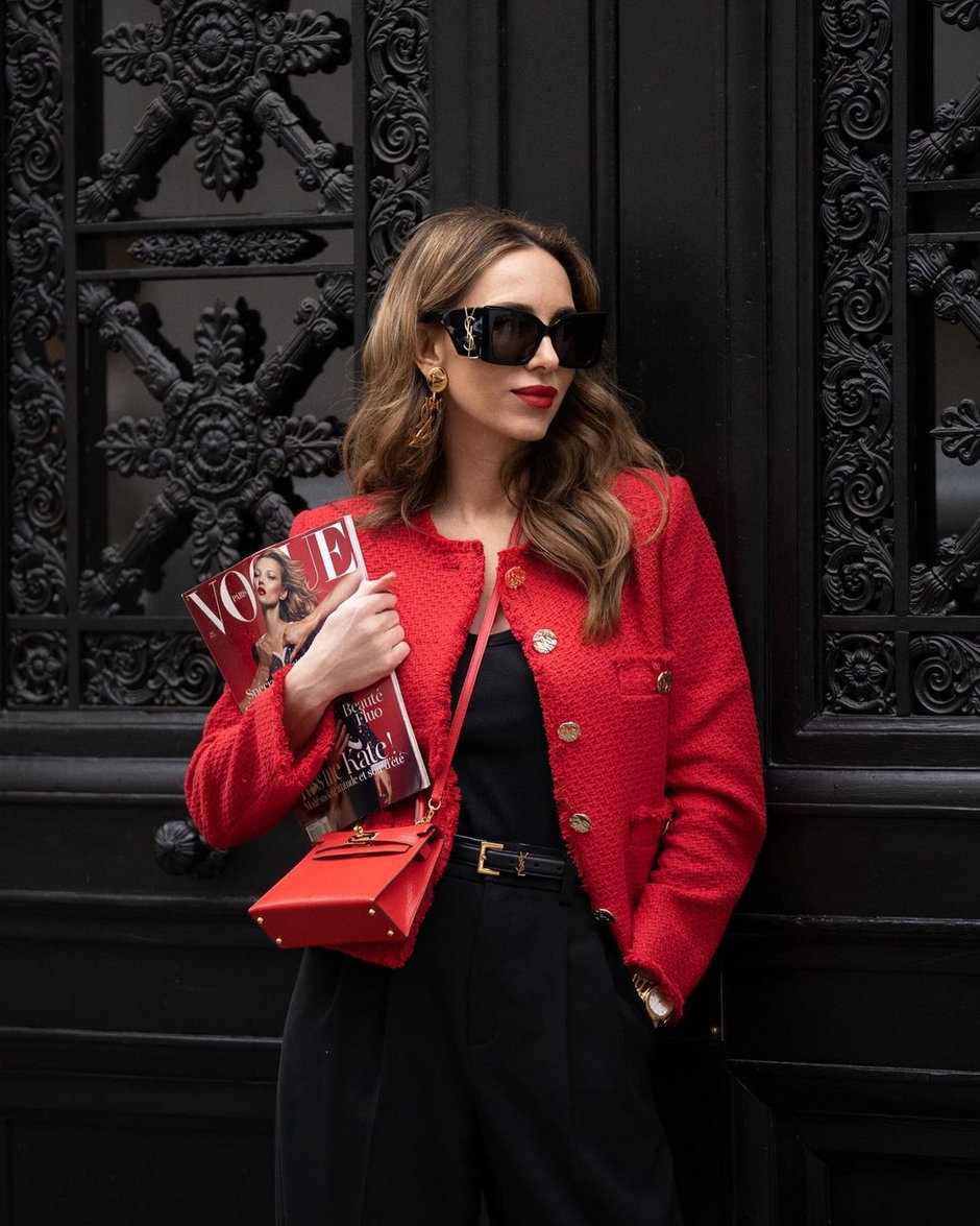 Kobieta w czerwonym żakiecie i okularach pozuje na tle drzwi z wydani