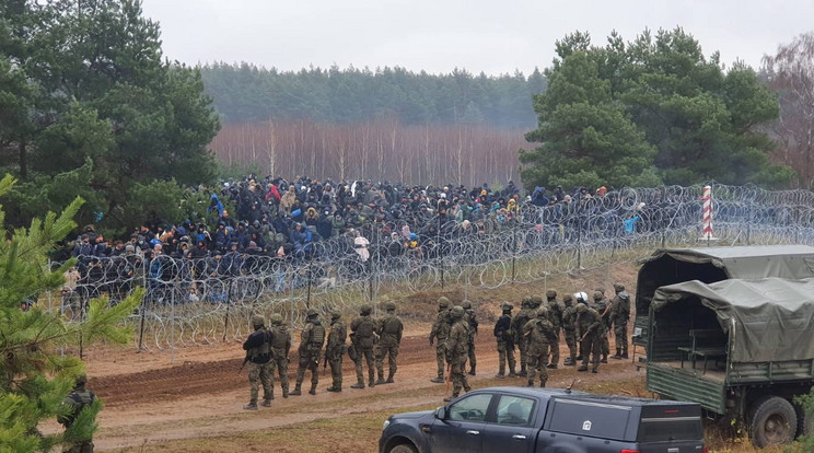 A lengyel 16. gépesített hadosztály által közreadott képen az Európai Unióba igyekvő migránsok a lengyel határt védő szögesdrótkerítés fehérorosz oldalán, az előtérben lengyel katonák a kelet-lengyelországi Kuznica térségében 2021. november 8-án. A lengyel-fehérorosz határon feszültség alakult ki a Fehéroroszország felől az Európai Unióba igyekvő több ezer migráns miatt. A lengyel hatóságok november 12-i becslése szerint 3-4 ezer migráns tartózkodik a fehérorosz-lengyel határ mentén, és a számuk folyamatosan gyarapodik / Fotó: MTI/EPA/Lengyel 16. gépesített hadosztály