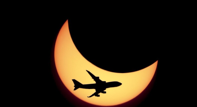 An airplane flies in front of the crescent of a solar eclipse.