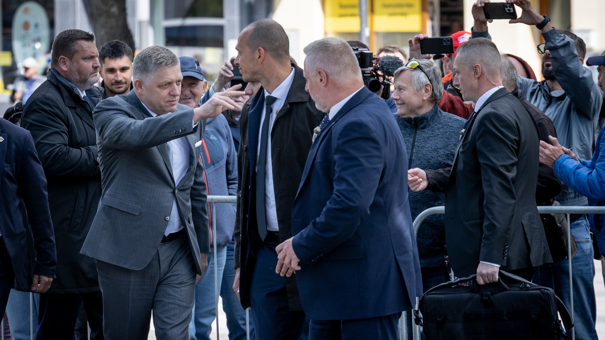 Robert Fico v obklopení policajtov z Úradu na ochranu ústavných činiteľov sa zdraví s ľuďmi na námestí v Handlovej rok po atentáte