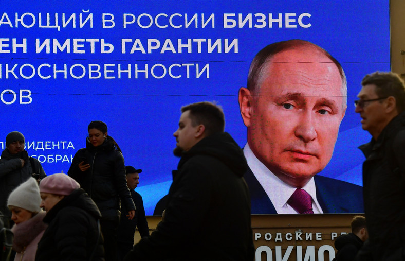 Ludzie przechodzący obok cyfrowego ekranu wyświetlającego wizerunek prezydenta Rosji Władimira Putina i cytat z jego niedawnego przemówienia do Zgromadzenia Federalnego w Sankt Petersburgu, 14 marca 2024 r.