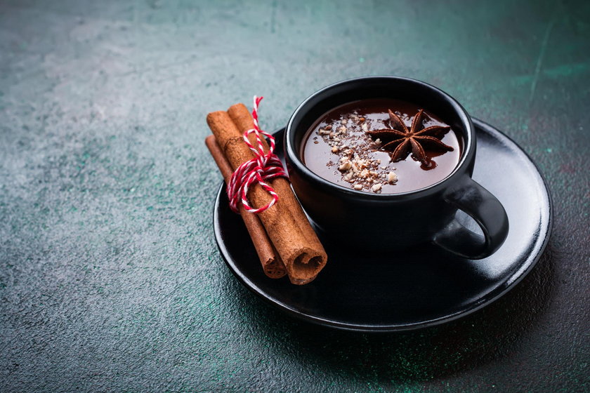 Hot chocolate with anise and nuts in black ceramic cup on old dark green concrete background. Select