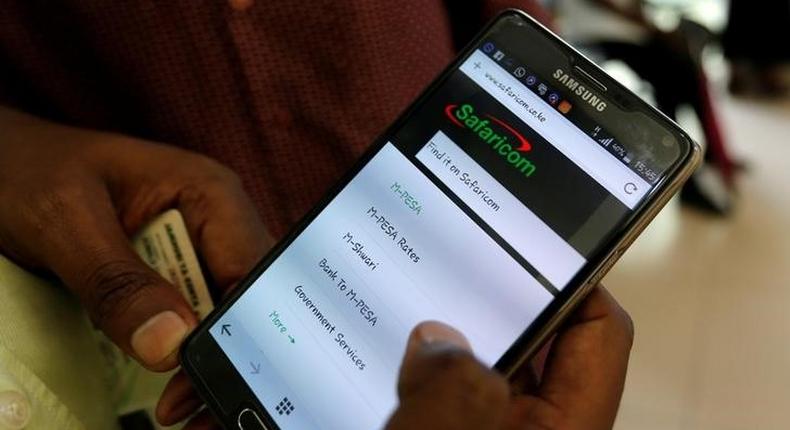 An employee assists a customer to set-up M-Pesa money transfer servive on his handset inside a mobile phone care centre operated by Kenyan's telecom operator Safaricom; in the central business district of Kenya's capital Nairobi, May 11, 2016. REUTERS/Thomas Mukoya