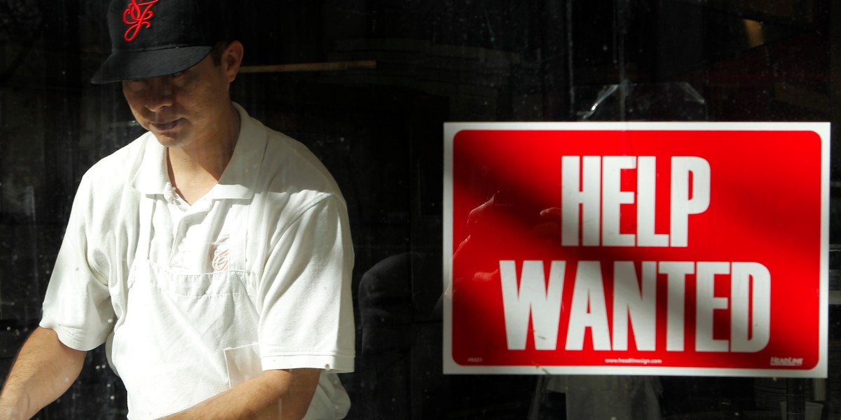 A man prepares a meal near a "help wanted" sign hanging in a restaurant window in San Francisco