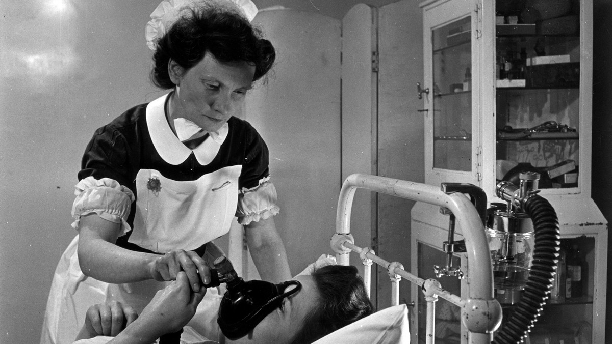 An expectant mother using an inhaler to take the pain killing drug trilene during labour, watched by a hospital midwife.