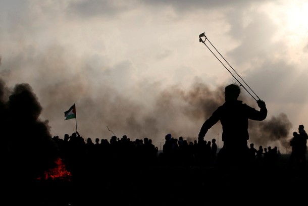 Palestinian demonstrator uses a sling to hurl stones towards Israeli troops during clashes, near the