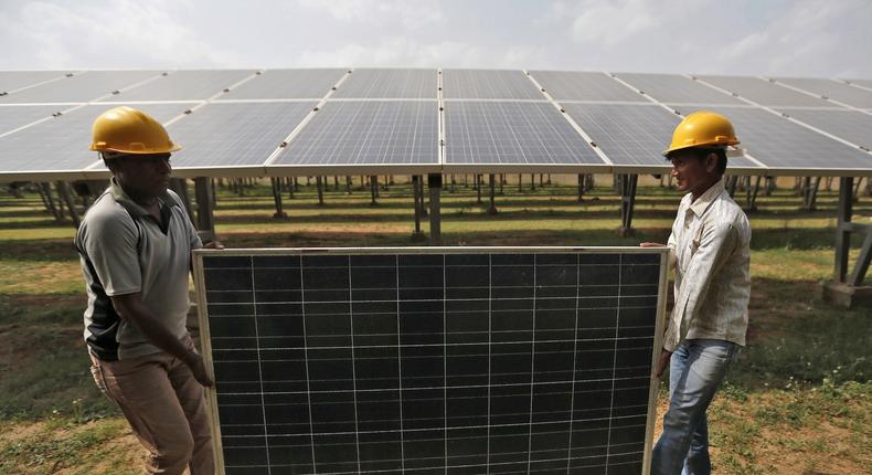 Workers carry a damaged photovoltaic panel inside a solar power plant in Gujarat.