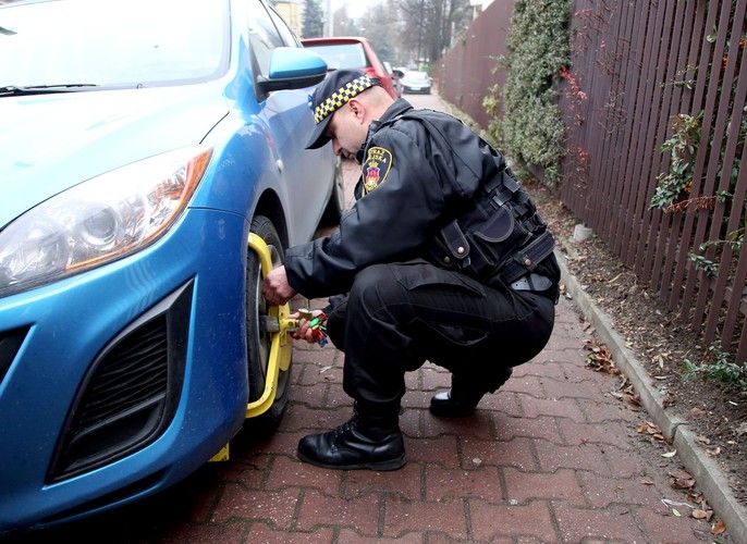 Straż miejska zakłada blokadę na źle zaparkowany samochód na ulicy Turystycznej w Krakowie. W tle volkswagen golf prezydenta Andrzeja Dudy