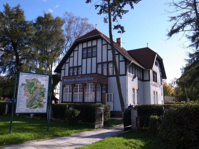 <strong>Język i kultura Kaszub</strong>
 <br></br>
Język kaszubski różnicuje się na 20 dialektów i dalej na 70 poddialektów. Barwy regionu to czarny i żółty. Obszar współczesnych Kaszub obejmuje 43 gminy województwa pomorskiego. Kaszubskie tradycje i język szczególnie żywe są w takich miastach jak: Wejherowo, Puck, Kartuzy, Żukowo, Kościerzyna, Szemud i Władysławowo. Czy stolicą Kaszub jest Wejherowo, Gdańsk, a może Kartuzy? Każda odpowiedź ma swoich zwolenników. O tym, czy dana miejscowość jest kaszubska, świadczy najczęściej obecność dwujęzycznych tablic.
<br></br>
Do miejsc, w których można zasmakować w Kaszubach szczególnie mocno należą m.in.: Muzeum Kaszubskie im. Franciszka Tredera w Kartuzach, Muzeum Piśmiennictwa i Muzyki Kaszubsko-Pomorskiej w Wejherowie, Muzeum Zachodniokaszubskie w Zamku w Bytowie oraz Kaszubski Park Etnograficzny we Wdzydzach Kiszewskich.
<br></br>
Sam język Kaszubów (kaszëbsczi jãzëk, kaszëbskô mòwa) to w istocie całe mnóstwo gwar, np. słowińska, kabacka, osiecka, żarnowiecka, żukowska, kartusko-goręczyńska, przywidzka, stężycka, lipuska, czy konarska. O tym jak brzmi mówiony kaszubski przekonać się można słuchając np. audycji kaszubskiego radia (radiokaszebe.pl).
<br></br>
Na zdjęciu: Muzeum Kaszubskie im. Franciszka Tredera w Kartuzach, fot. M_H.DE, licencja CC-BY-SA