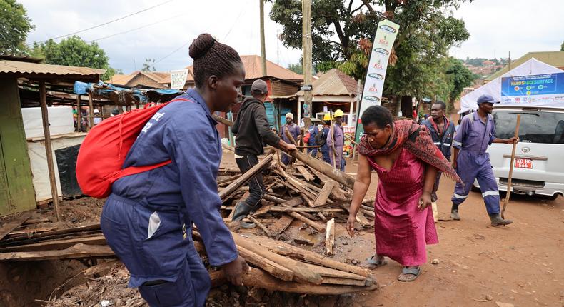 A local leader joins a KCCA worker to remove debris from a drainage channel
