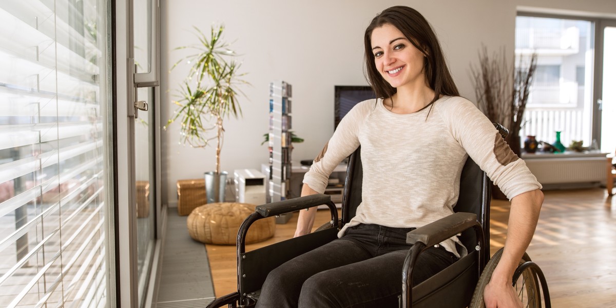 Young disabled woman in wheelchair at home in living room.