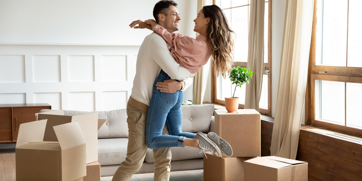 Happy husband lifting excited wife celebrating moving day with boxes