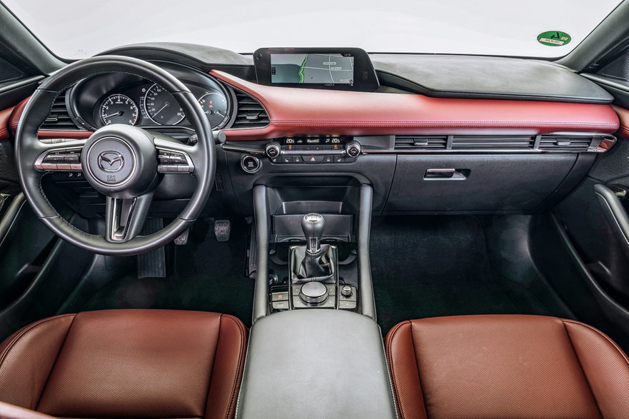 Mazda 3: skórzany element stylistyczny w sumiennie zmontowanym kokpicie, który jakością puka do drzwi klasy premium. W centrum ręczna skrzynia i pokrętło do sterowania centralnym ekranem.