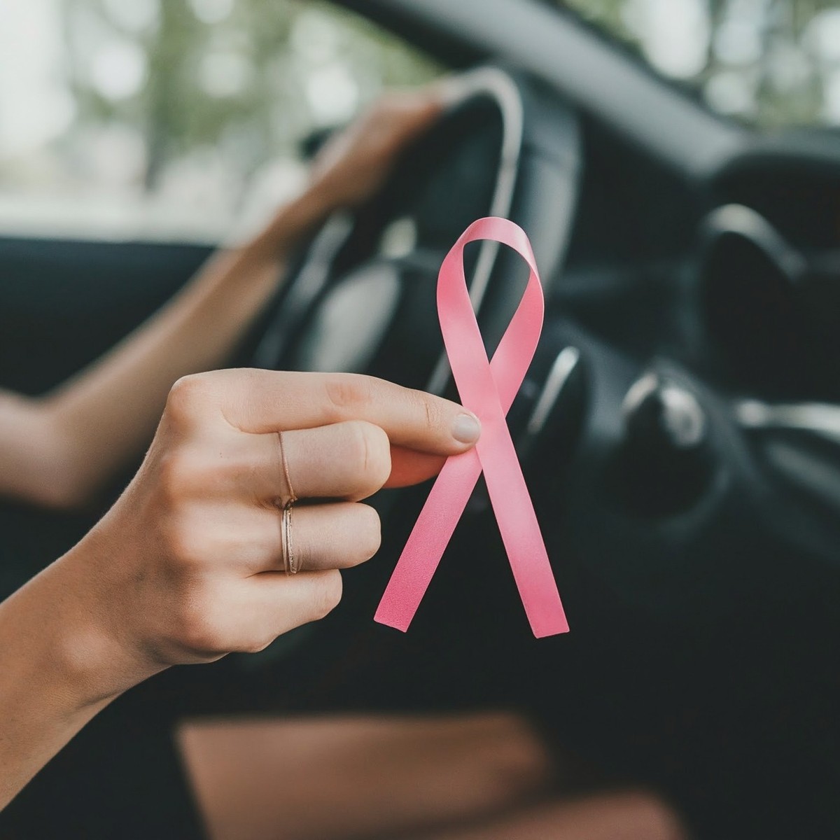 Kobieta za kierownicą auta z różową wstążką w dłoni