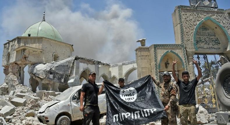 Iraqi soldiers pose with an upside-down flag of the Islamic State group outside the ruins of the Nuri mosque in the Old City of Mosul on June 30, 2017