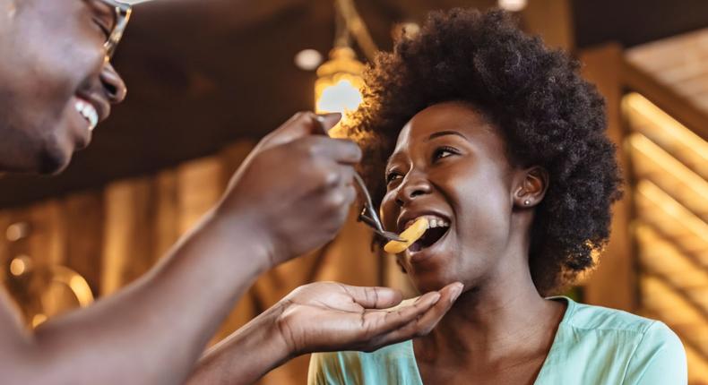 Happy man sharing French fries and feeding his girlfriend while having lunch in a restaurant.